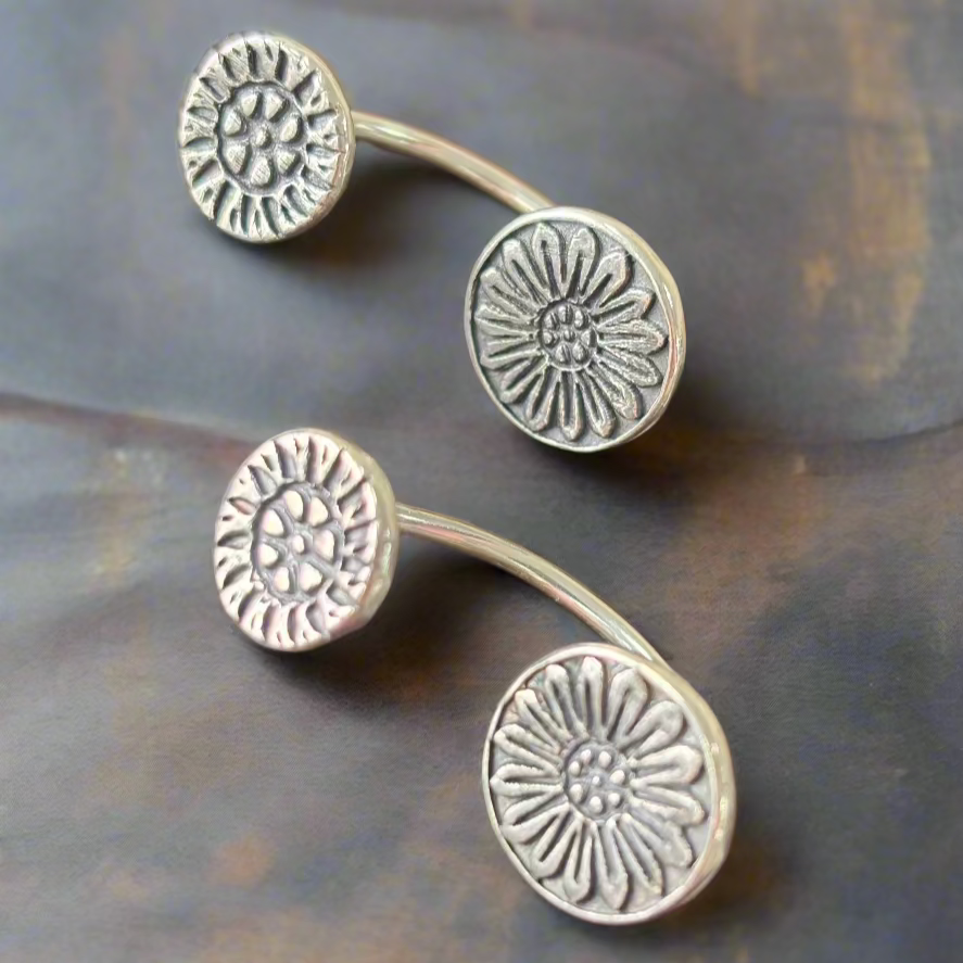 Pair of silver floral earrings on a textured surface. Class with Carrie Story. Online or In Person